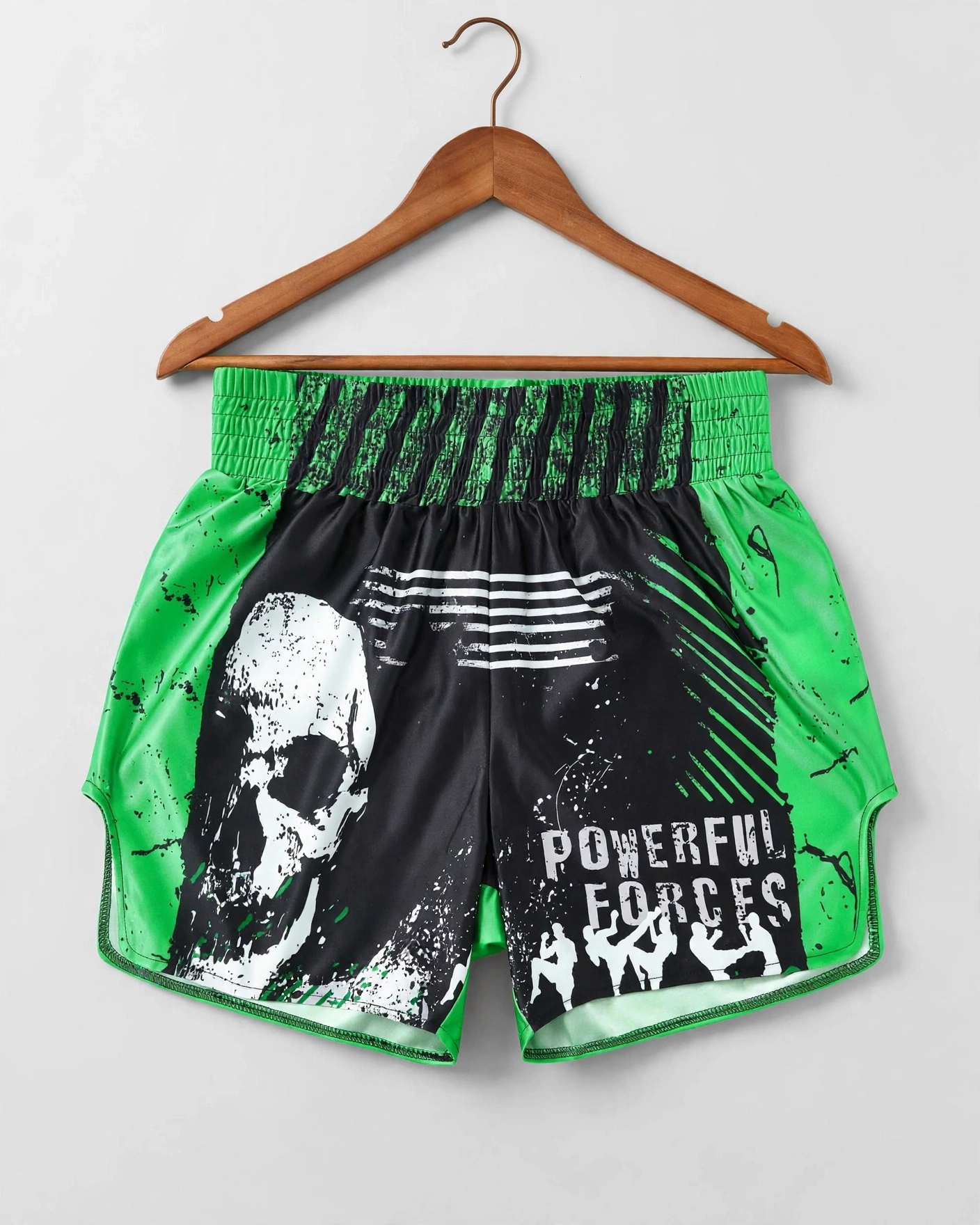 Green and black Muay Thai shorts with white skull and Powerful Forces text hanging on wooden hanger - 423x509 tech pack design submission